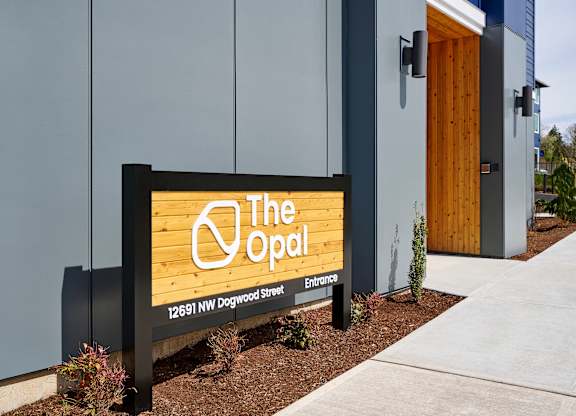 A signboard with the text "The Opal" and an address "12691 NW Dogwood Street" is displayed in front of a building.