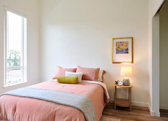 A bedroom with a pink bedspread and a grey blanket.