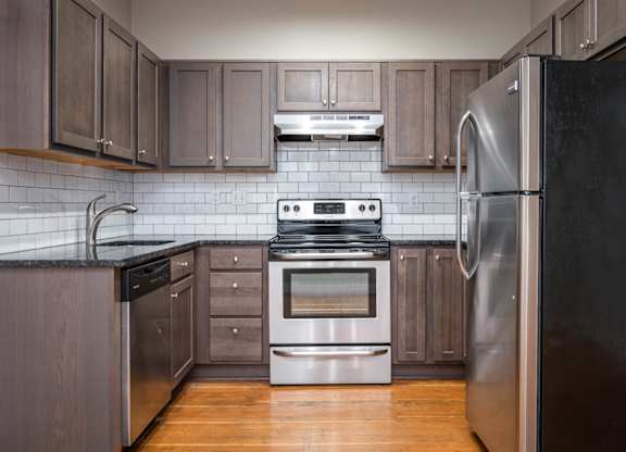A modern kitchen with a stainless steel refrigerator, stainless steel appliances, and wooden cabinets.