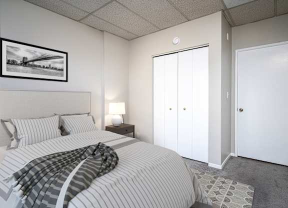 A bedroom with a bed, a lamp, a picture on the wall, and a plant.
