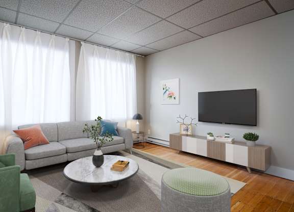 A living room with a grey sofa, a green armchair, a grey coffee table, a grey side table, a white wall, a black TV, a white curtain, and a grey floor.