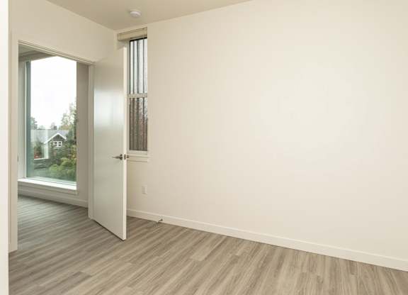 A room with a white door and a window with a view of a house and trees outside.