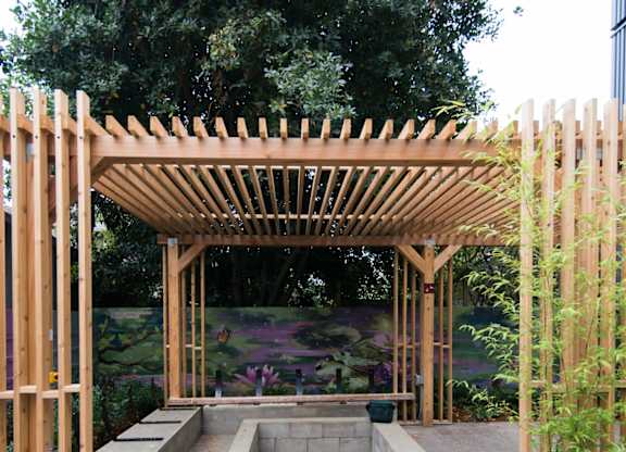 A wooden pergola with a concrete floor and a small fountain in the middle.