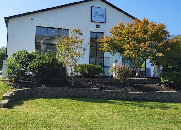 the front of a white building with a lawn and trees at Schaefer Ridge Apartments, Branson , MO