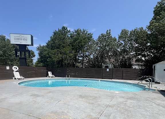 a swimming pool at a hotel with a fence and trees at Schaefer Ridge Apartments, Missouri