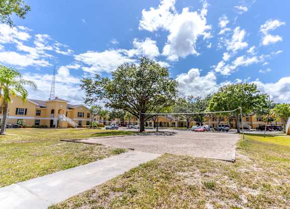 A playground with a volleyball net and a basketball hoop is surrounded by buildings and trees.