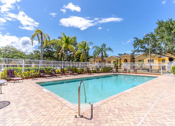 A pool surrounded by a white fence and palm trees.