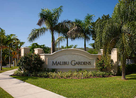 a sign gardens in front of palm trees