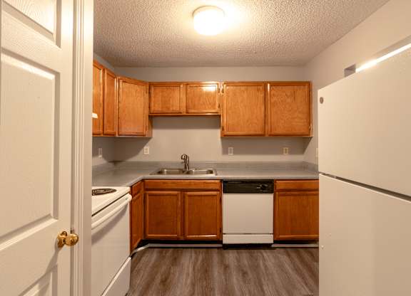 an empty kitchen with white appliances and wooden cabinets at Avon Crossings, Durham, NC 27713