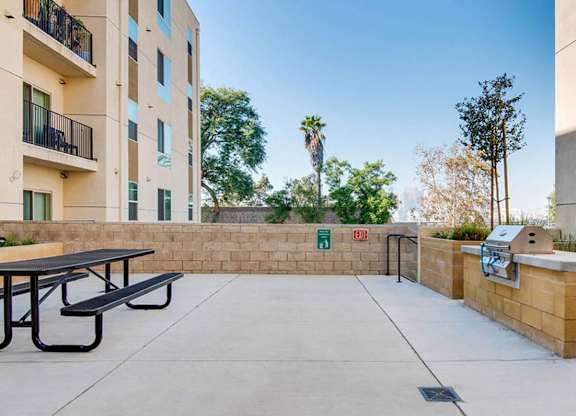A concrete patio with a table and chairs is surrounded by a wall and a building with balconies.