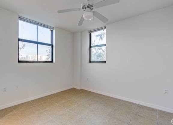A room with a ceiling fan and two windows.