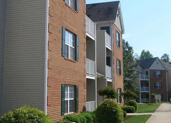 Apartment building with a white fence and green bushes in front.