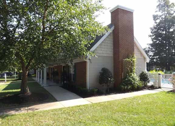 A small church with a red brick chimney is surrounded by a white picket fence and green trees.