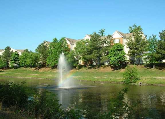 A fountain in the middle of a pond with a rainbow effect.