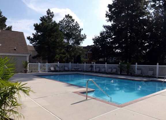 A pool surrounded by a white fence and trees.