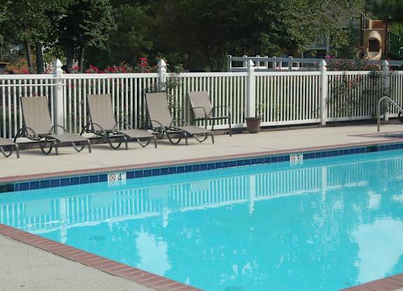 A pool with a white fence and chairs around it.
