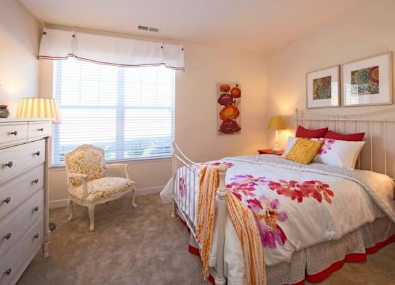 A bedroom with a bed, chair, and nightstand.