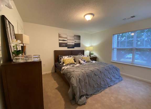 A bedroom with a bed, nightstand, and a window with blinds.