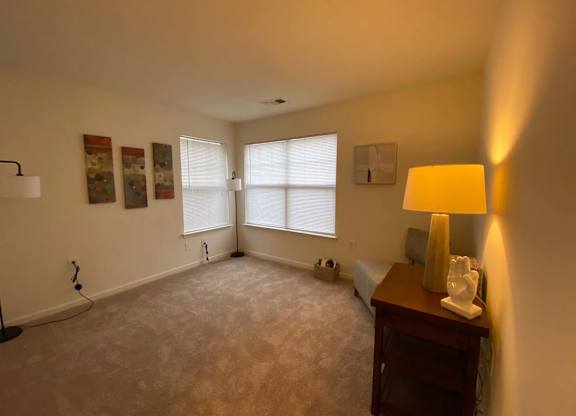 A room with a carpet floor, a lamp, a bed, and a window.