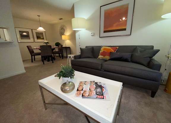 A living room with a grey couch, a white coffee table, and a painting on the wall.