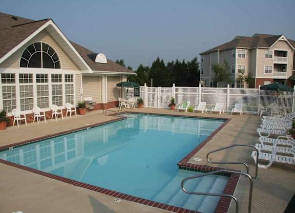 A swimming pool surrounded by a white fence and chairs.