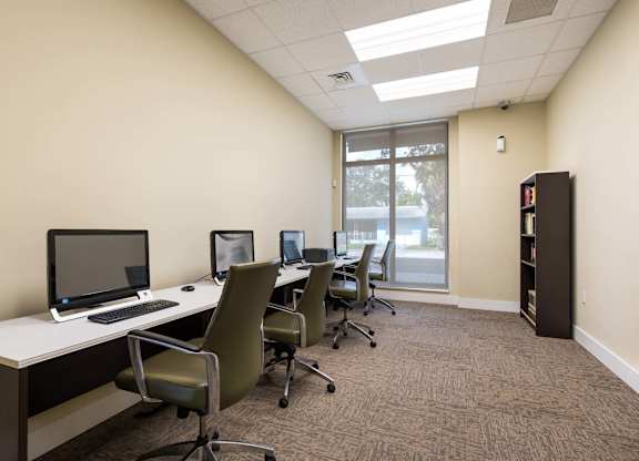 A room with a desk, chairs, and computers.
