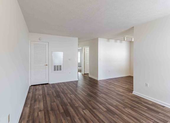 A room with white walls and wooden flooring with a door on the left.