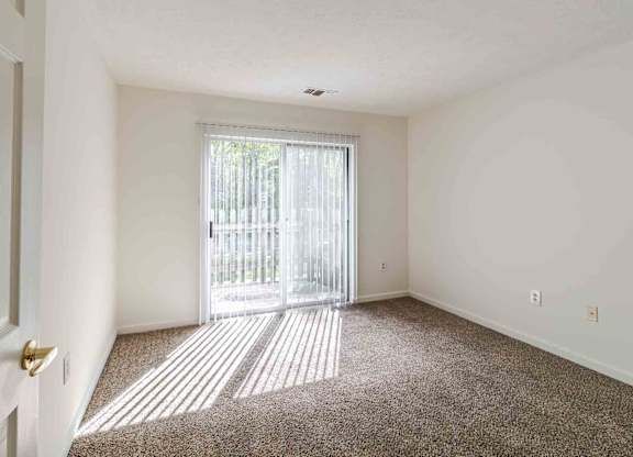 A room with a carpeted floor and a sliding glass door leading outside.