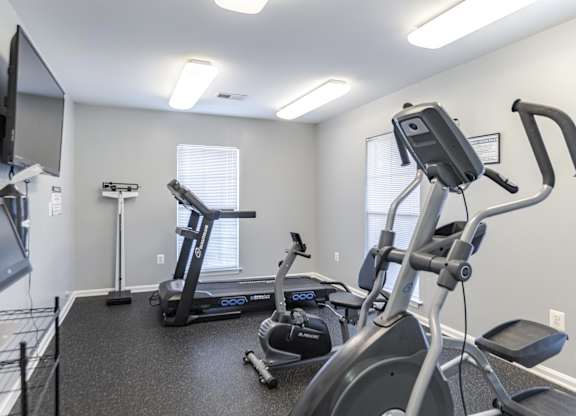 A spacious gym with a treadmill, elliptical trainer, and a television at English Oaks Apartments, Virginia, 22406