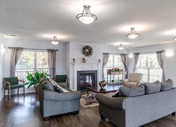 A living room with a grey couch, a green chair, and a fireplace at English Oaks Apartments, Virginia