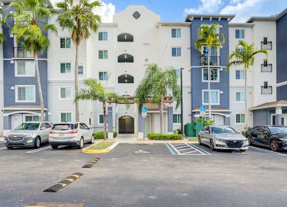 A parking lot in front of a multi-story building with cars parked.