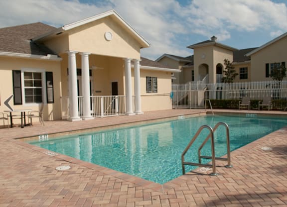 A pool in front of a house with a white fence.