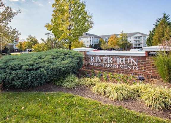 A sign for River Run Senior Apartments is surrounded by shrubbery.