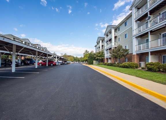 A long street with cars parked on the side and apartment buildings on the other side.