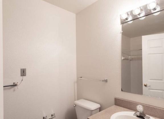 A bathroom with a toilet, sink, mirror, and lighting fixture.