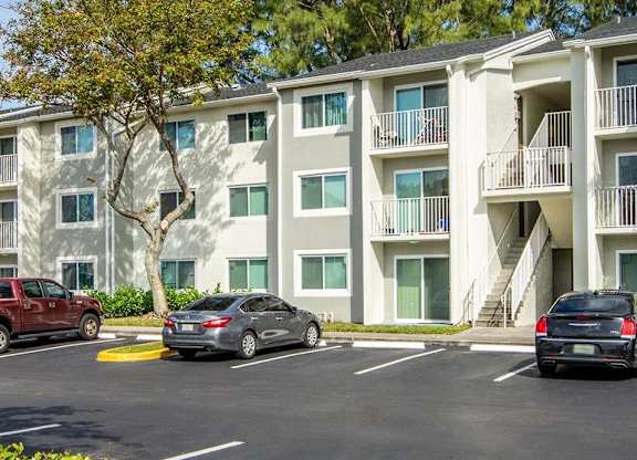 A parking lot in front of a multi-story apartment building with cars parked in the spaces.