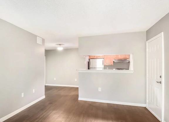 A room with a white door and a window with a view of a kitchen.