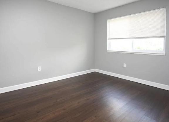 A room with wooden flooring and a window with blinds.