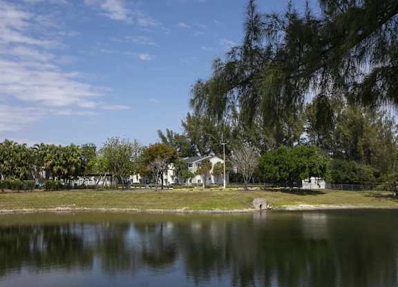 A serene lake with a house and trees in the background.
