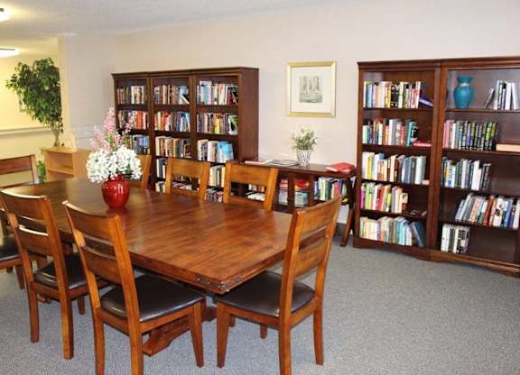 a library with a wooden table and chairs and bookshelves at Greenbrier Seniors Apartments, Chesapeake, VA  