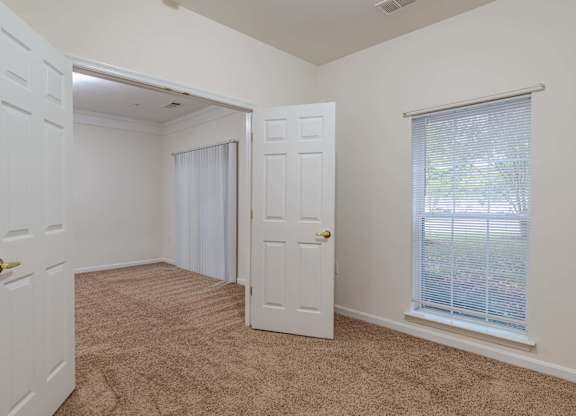 A room with a carpeted floor, a window with blinds, and a door.