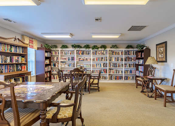 A room filled with wooden chairs and tables with a bookshelf in the background.