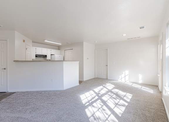 the living room and kitchen of an apartment with white walls and carpet