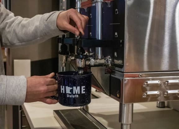 a person making a cup of coffee in a coffee machine at Bluestone Lofts, Minnesota, 55803