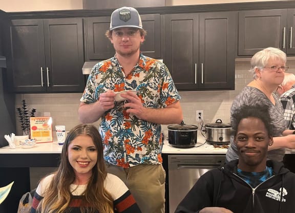 a group of people standing in a kitchen holding plates of food  at Timber Ridge, Forest Lake, MN