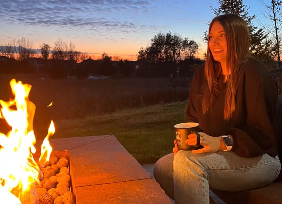 a woman sitting next to a fire with a cup of coffee  at Timber Ridge, Forest Lake, 55025