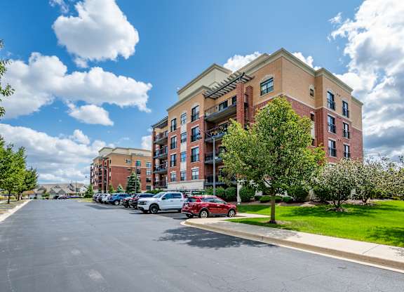 A red car is parked on the side of a street in front of a large apartment building.