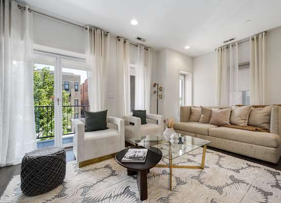 A living room with a white sofa, a black ottoman, and a glass coffee table.