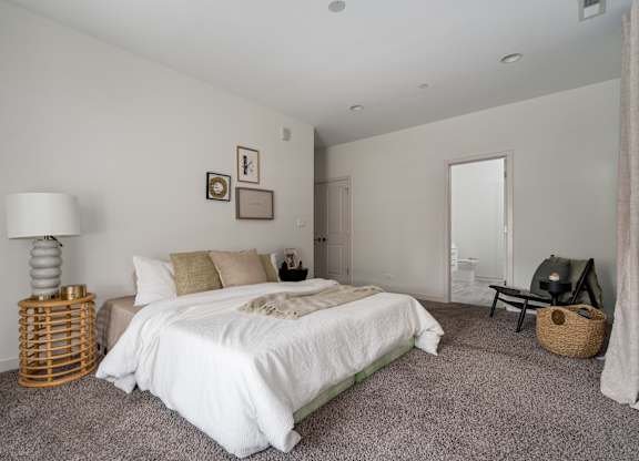 A bedroom with a white bed and a grey carpet.