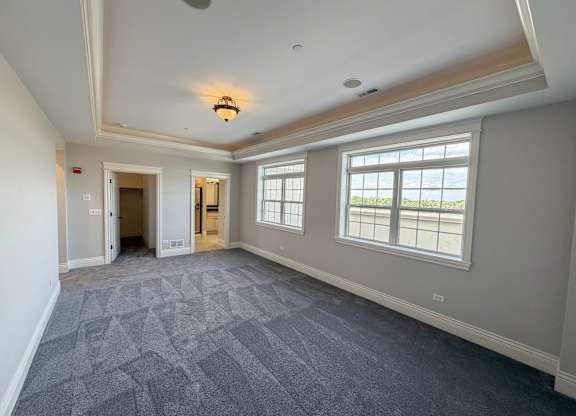 A large empty room with a patterned carpet and a window overlooking the sea.